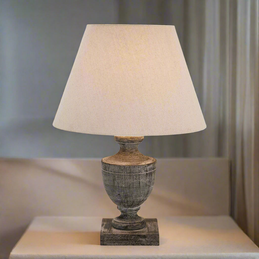 a bold wooden table lamp with a grey-wash patina and soft linen shade in dramatic lighting