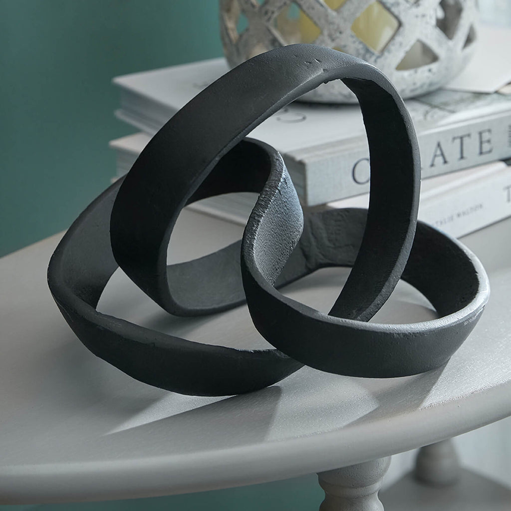 Black aluminum sculptural knot ornament with sleek curves, creating striking geometric shadows in modern dÃ©cor by sostter at brixbailey.com