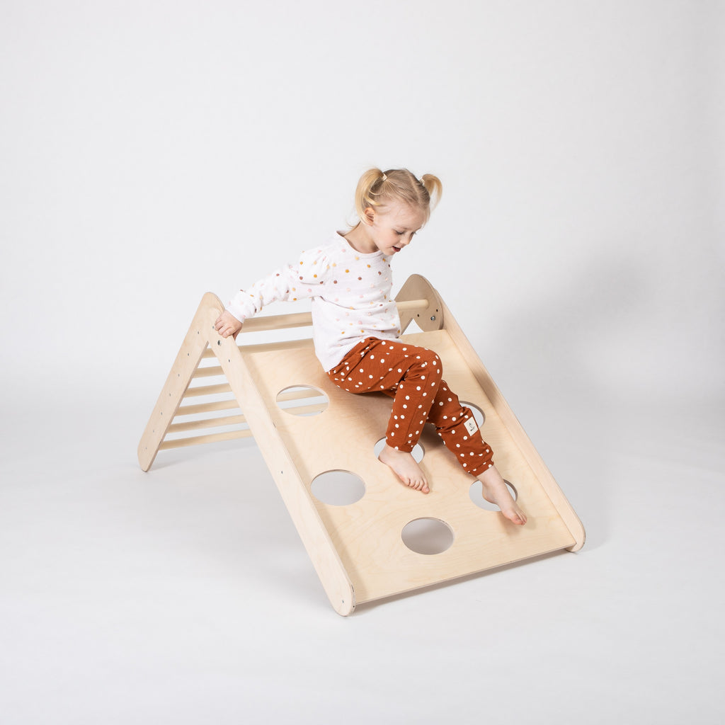 foldable montessori climbing triangle in a sunlit playroom, toddler gripping the sturdy birch rungs with determination