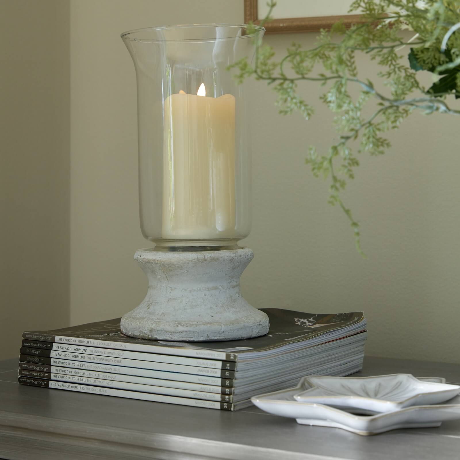 Handcrafted cream hurricane lantern with stone-effect base and antiqued patina, casting warm LED candlelight glow. by sostter at brixbailey.com