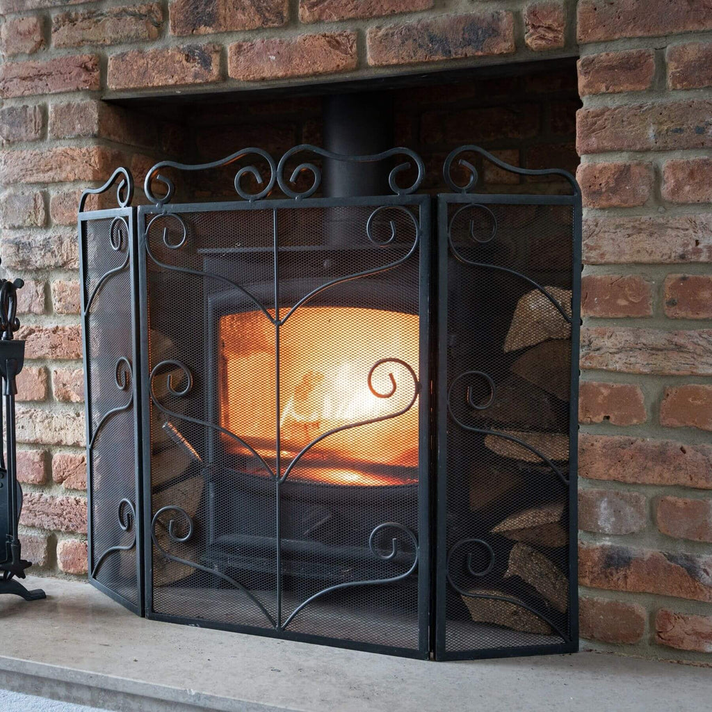 Black ornate metal fire screen with intricate design, protecting hearth in classic matte finish by Sostter at brixbailey.com