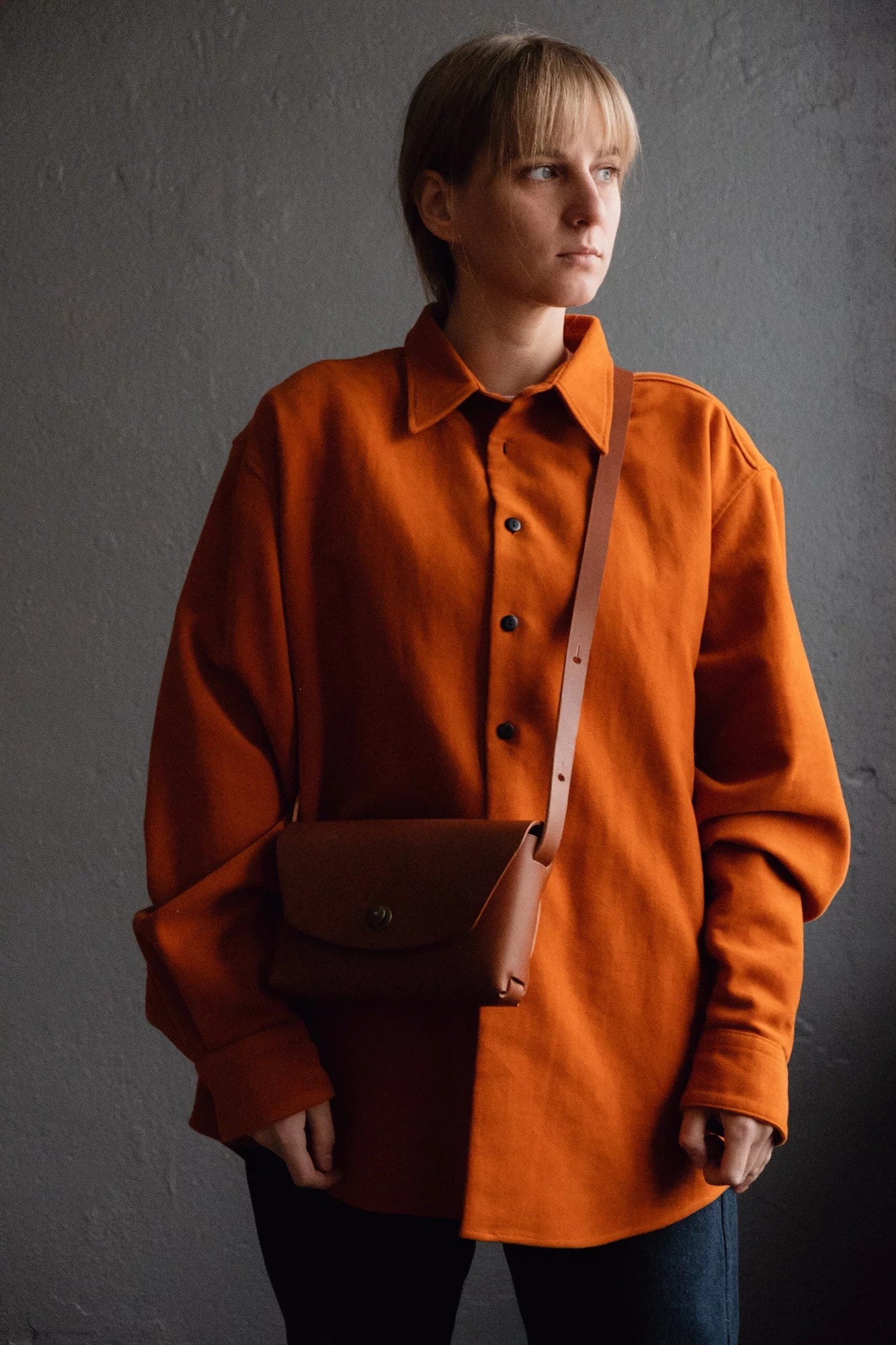 playful rust brown leather clutch held against a bright, sunny backdrop