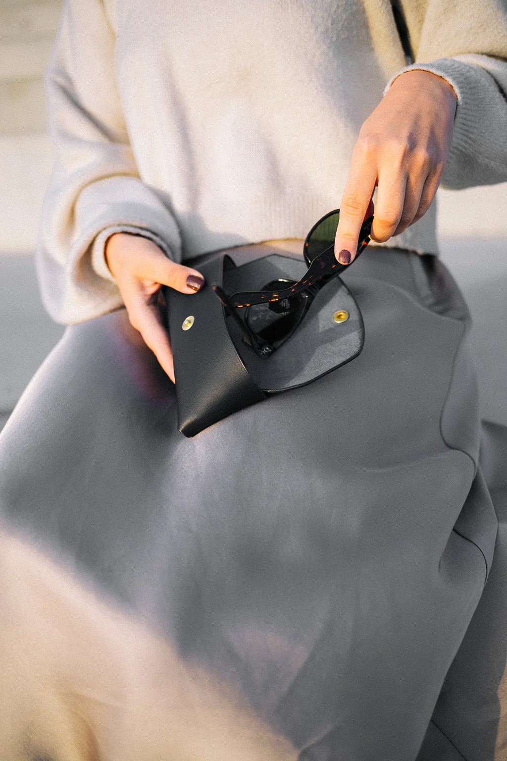 softly lit black leather sunglasses case resting on a cozy surface, open to reveal its plush protective interior lining