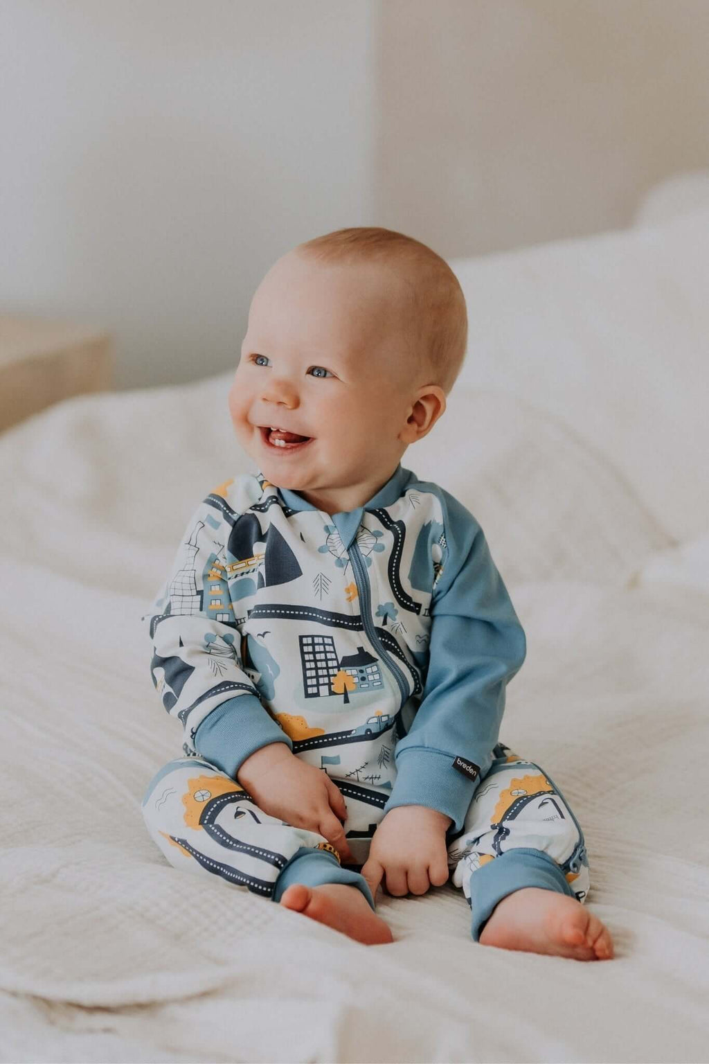 a soft cotton baby sleepsuit in a gentle city life print, with cozy ribbed cuffs and a two-way zipper for easy changes