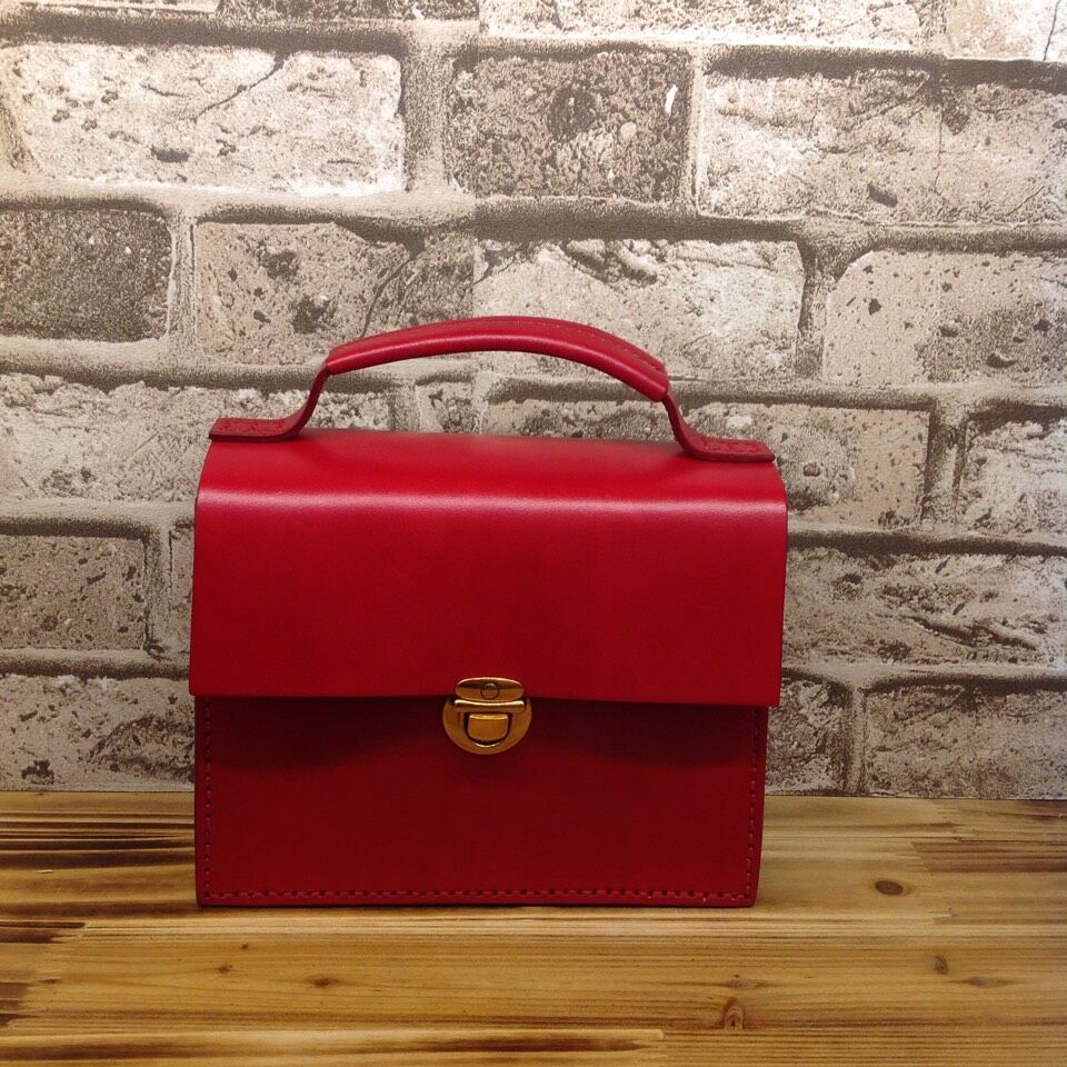 Red leather briefcase on a wooden surface with a stone wall background
