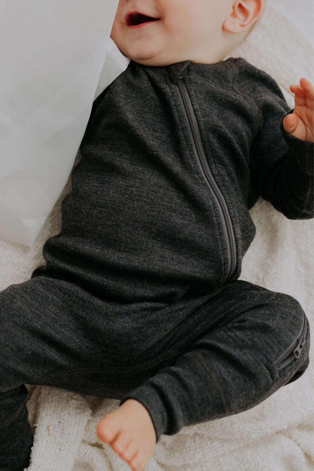 soft merino wool baby jumpsuit in a cozy nursery setting, side view showing the smooth two-way zipper