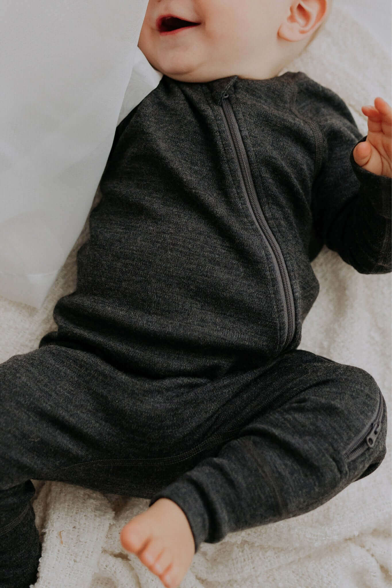 soft merino wool baby jumpsuit in a cozy nursery setting, side view showing the smooth two-way zipper