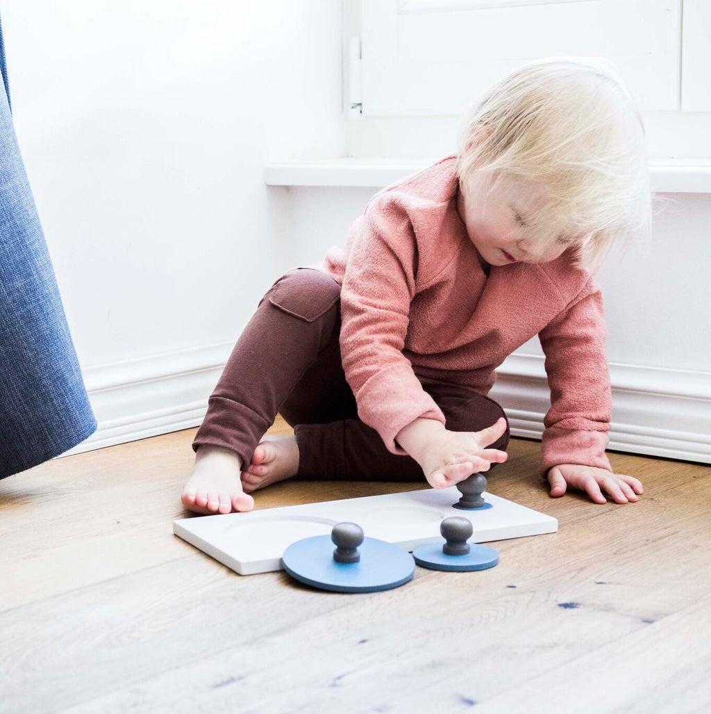 a child's hand playing with a colorful montessori circle puzzle on a sunny wooden floor