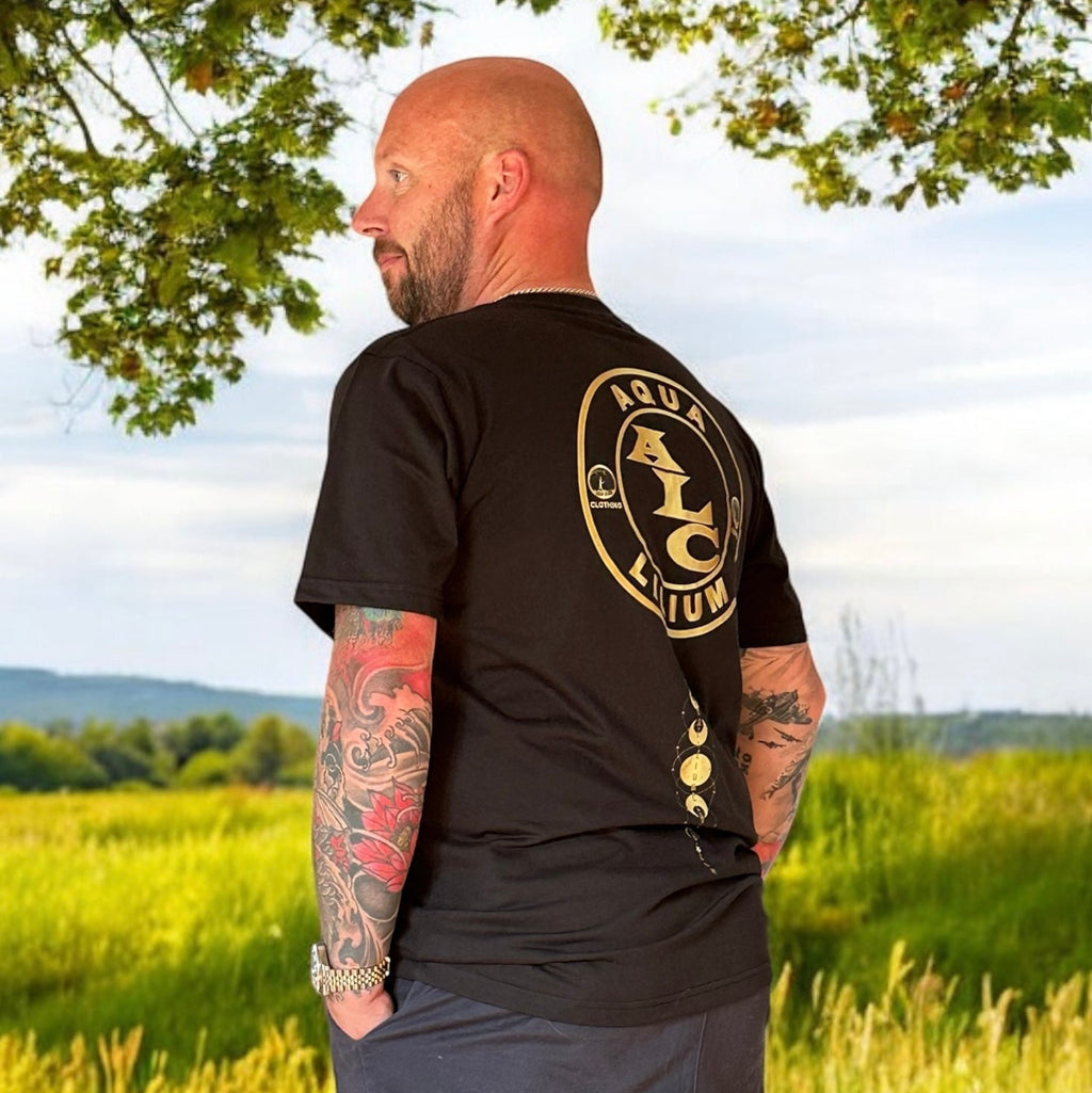 Man wearing a black t-shirt with a logo standing in a grassy field sostter.pro