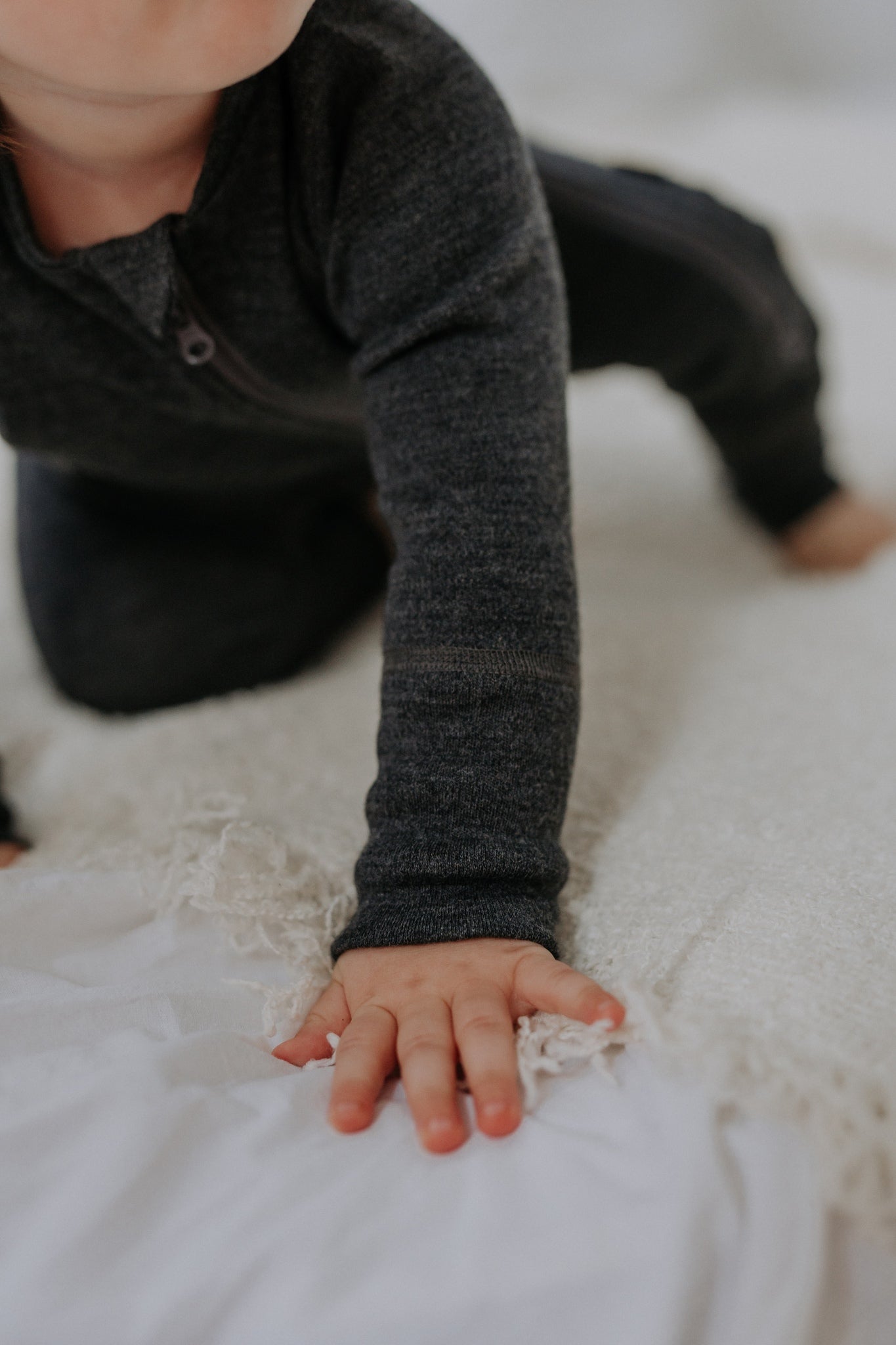 a happy baby playing in a soft mulesing-free merino wool jumpsuit with a two-way zipper