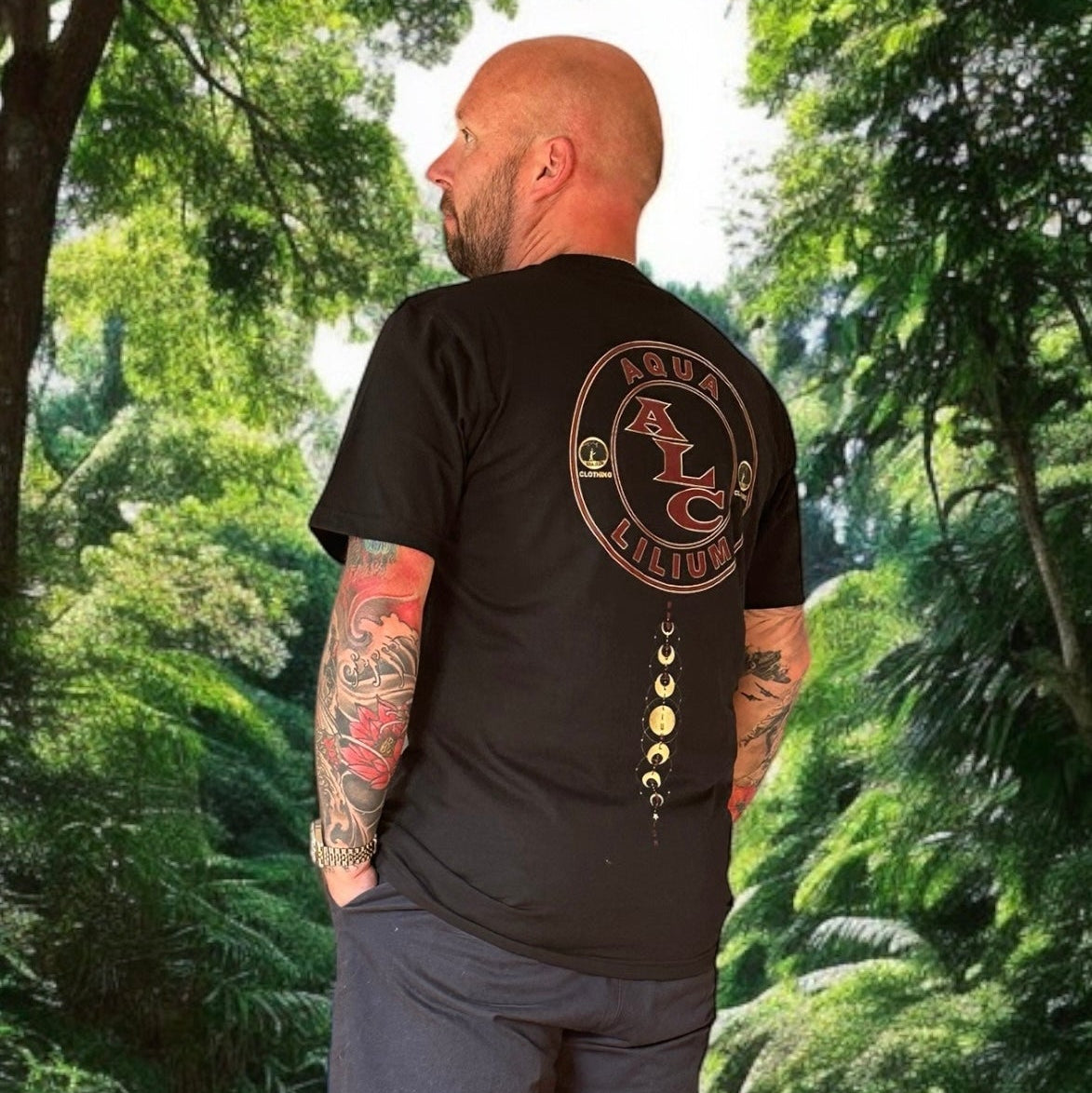 Man wearing a black t-shirt with a logo on the back, standing in a forest on sostter.pro