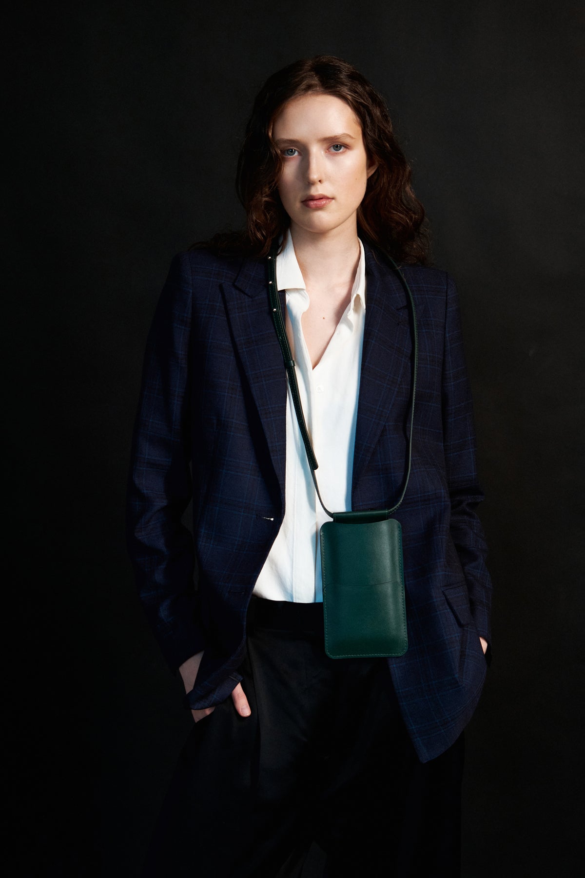 confident woman wearing a forest green leather crossbody phone bag against an urban backdrop