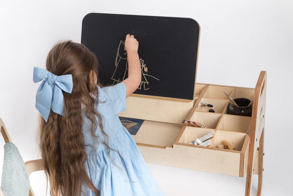 a child's drawing on the mint green montessori table with art supplies neatly stored