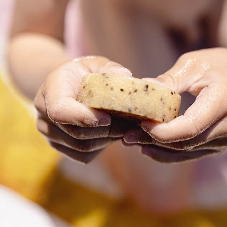 close-up of kiwi seed scrub bar with lemongrass scent, playful texture on wet skin