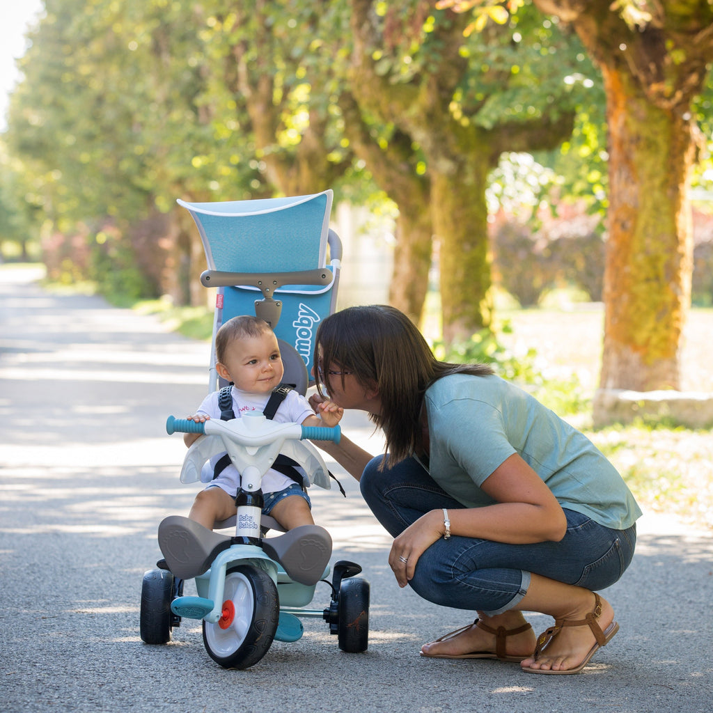 blue smoby baby balade plus tricycle with sun visor and storage bag in playful outdoor setting
