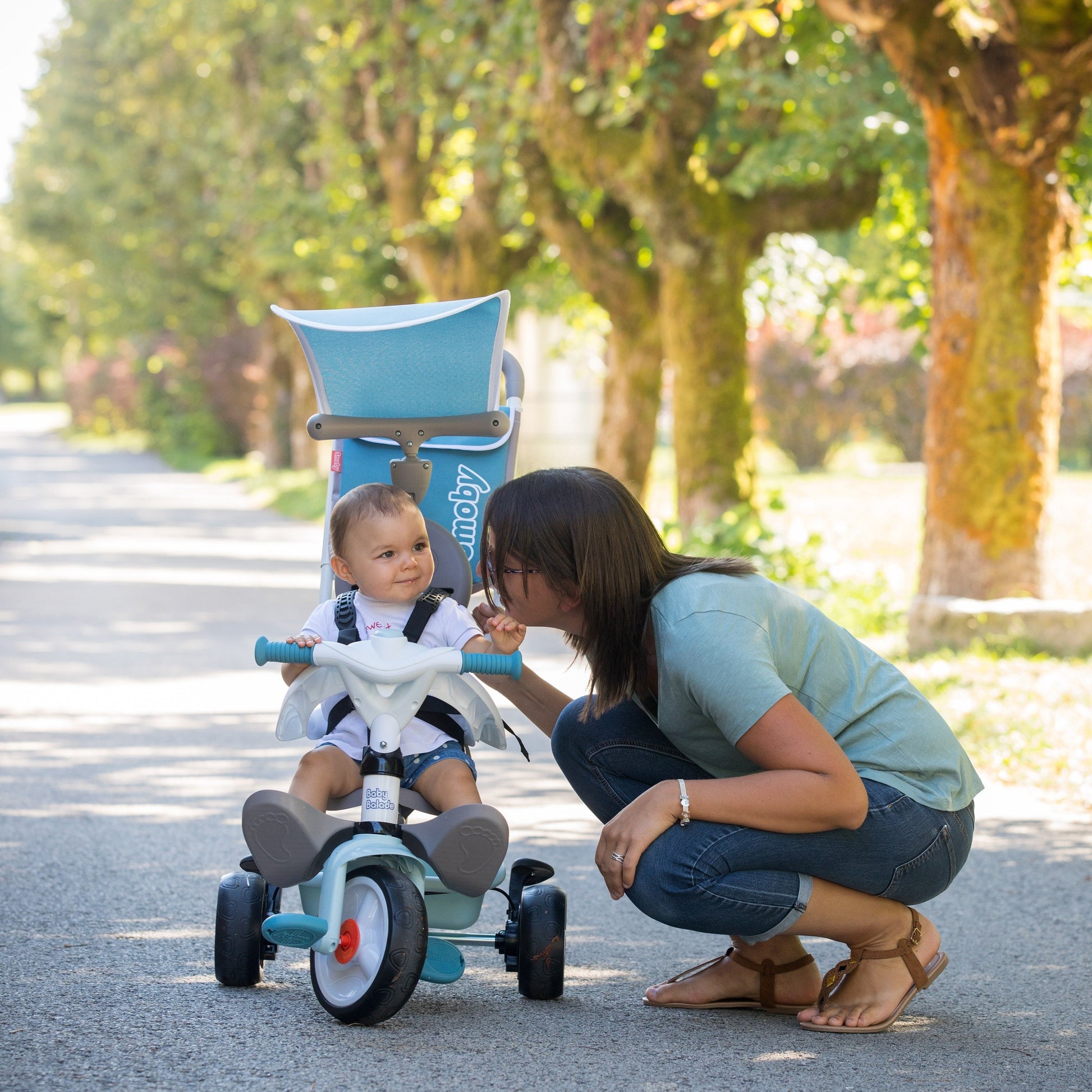 blue smoby baby balade plus tricycle with sun visor and storage bag in playful outdoor setting