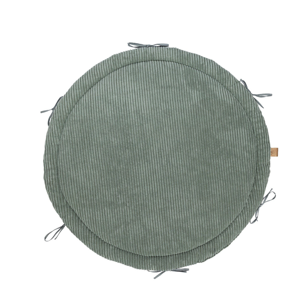 soft olive green baby nest with braided bumper on a cozy nursery rug
