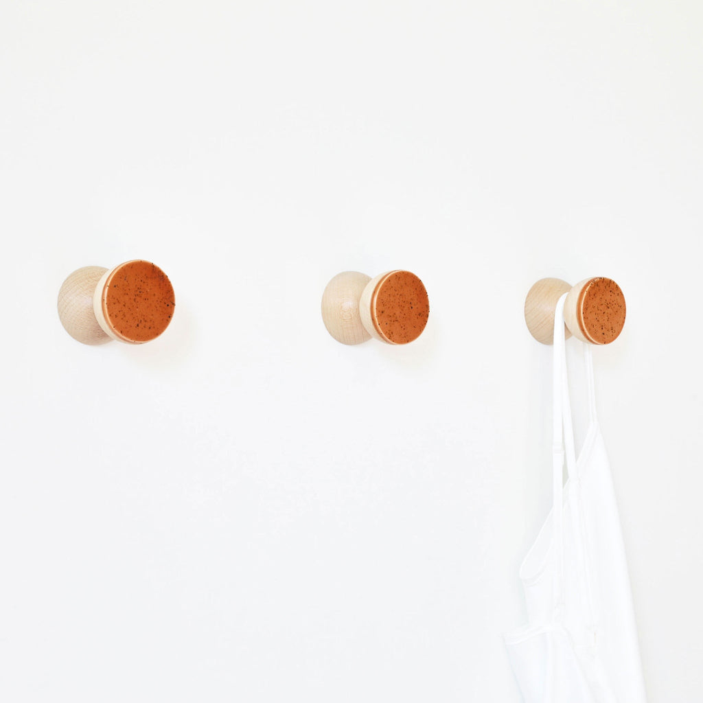 bold terracotta-speckled ceramic wall hook on beech wood in dramatic studio lighting