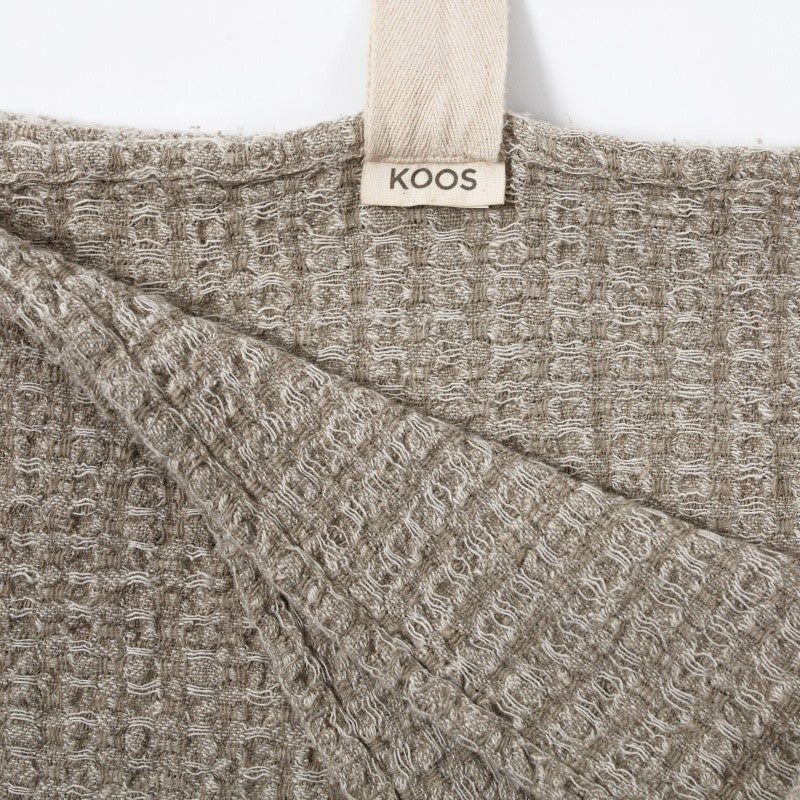 a textured grey linen bath towel hanging on a wooden hook in soft morning light