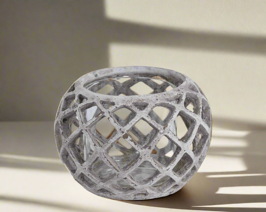 Handcrafted ceramic hurricane lantern with geometric lattice design, casting mesmerizing light patterns in neutral stone finish. by Sostter at brixbailey.com