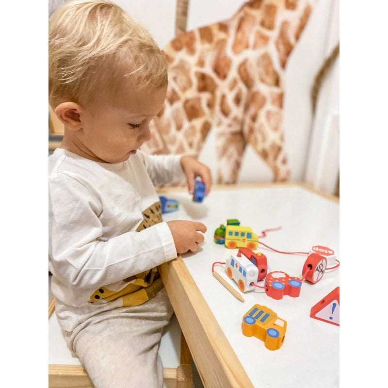 a child's hand threading a string through a wooden fire truck block on a natural wood table