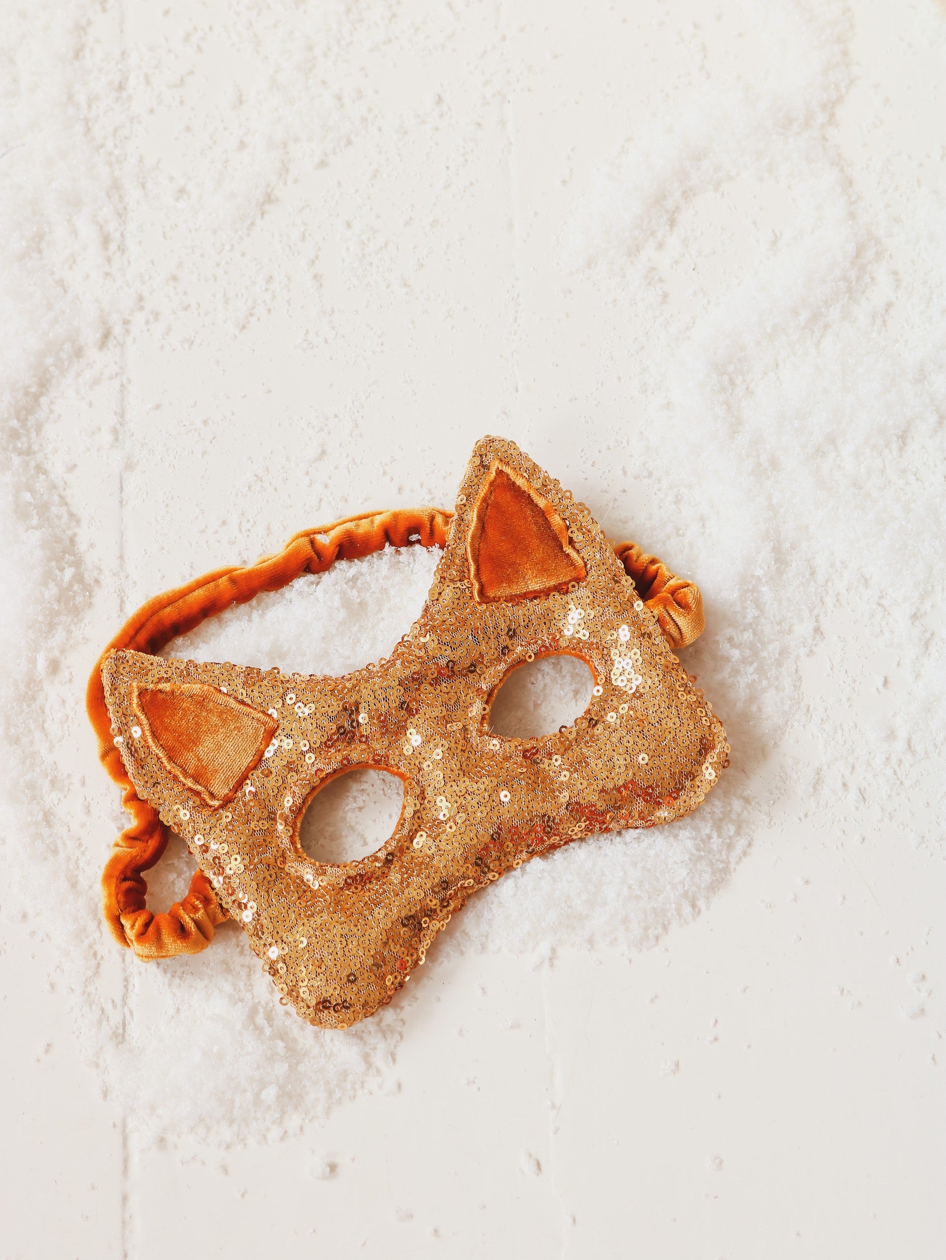 a child's hand holding a glittery gold cat mask with soft velvet and sparkling sequins