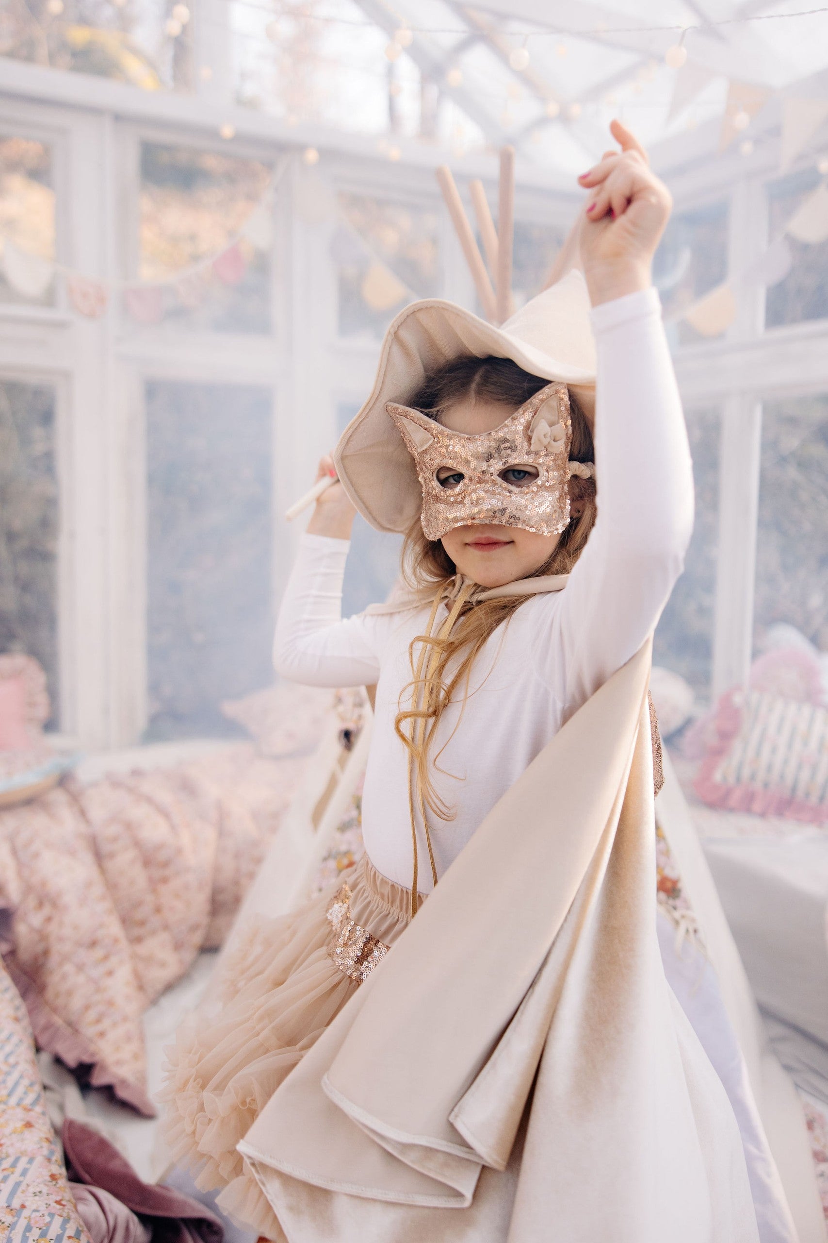 a playful toddler wearing a rose gold sequin cat mask, laughing during a birthday party