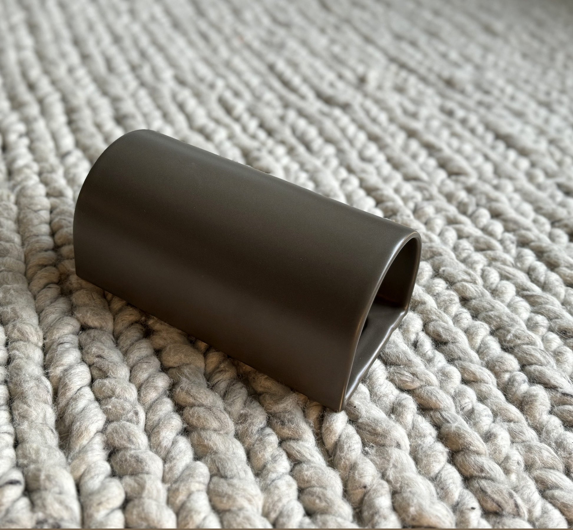 elegant handcrafted ceramic wall light in warm brown, showcasing its refined curve and unique glaze texture in a soft, intimate glow