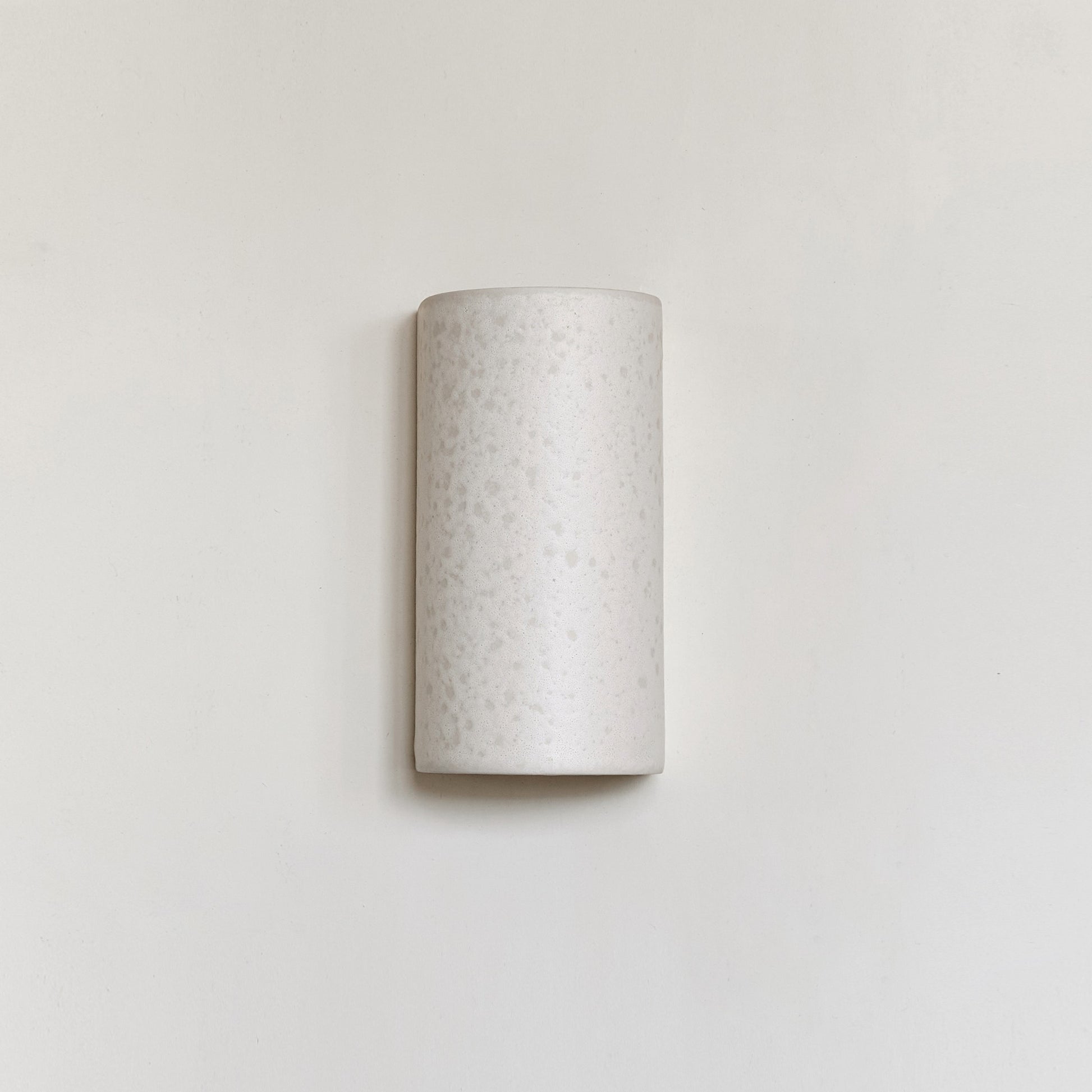 elegant handmade ceramic wall light in raw white, casting a soft glow against a minimalist background