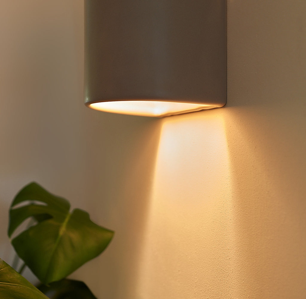 handmade taupe ceramic wall light mounted on a hallway wall, demonstrating its practical glow and dimensions