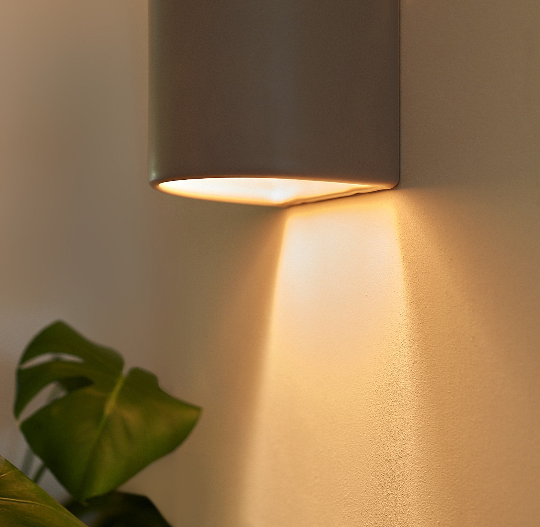 handmade taupe ceramic wall light mounted on a hallway wall, demonstrating its practical glow and dimensions