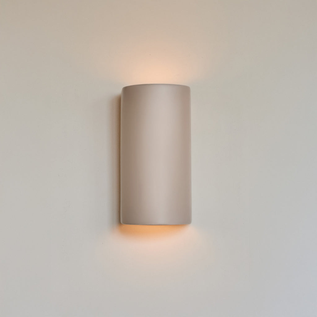 handmade taupe ceramic wall light casting a soft, functional glow in a nursery