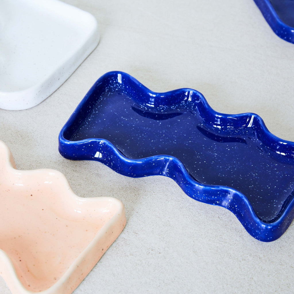 blue speckled ceramic wave tray on a wooden table, sunlight highlighting its playful texture