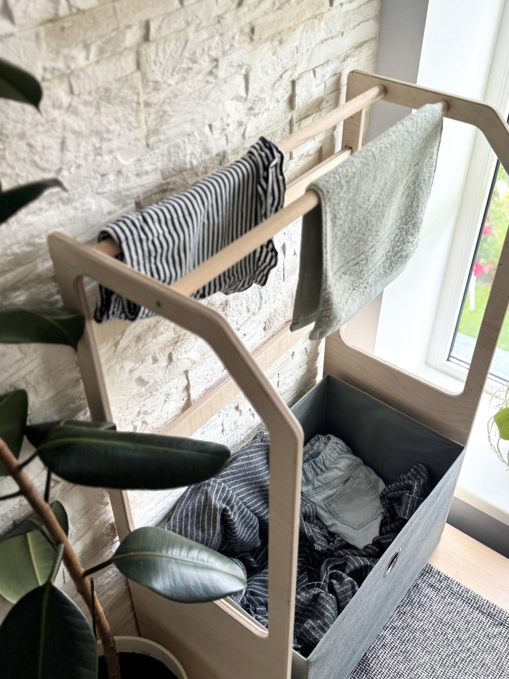 a sophisticated kids wooden drying rack with a green fabric basket in a minimalist nursery