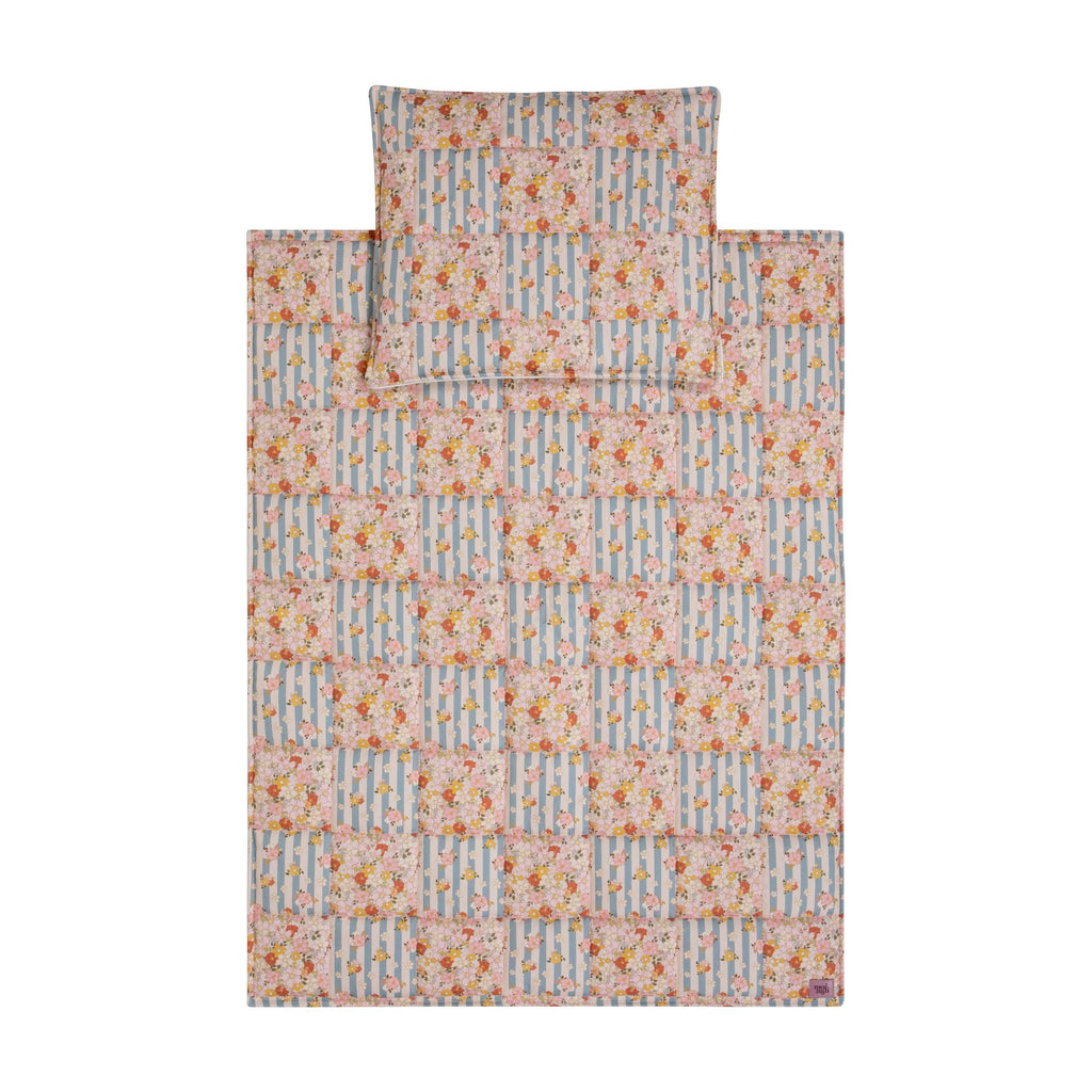 soft cotton quilted patchwork blanket and pillow set in summer garden print, laid out on a wooden floor with natural sunlight