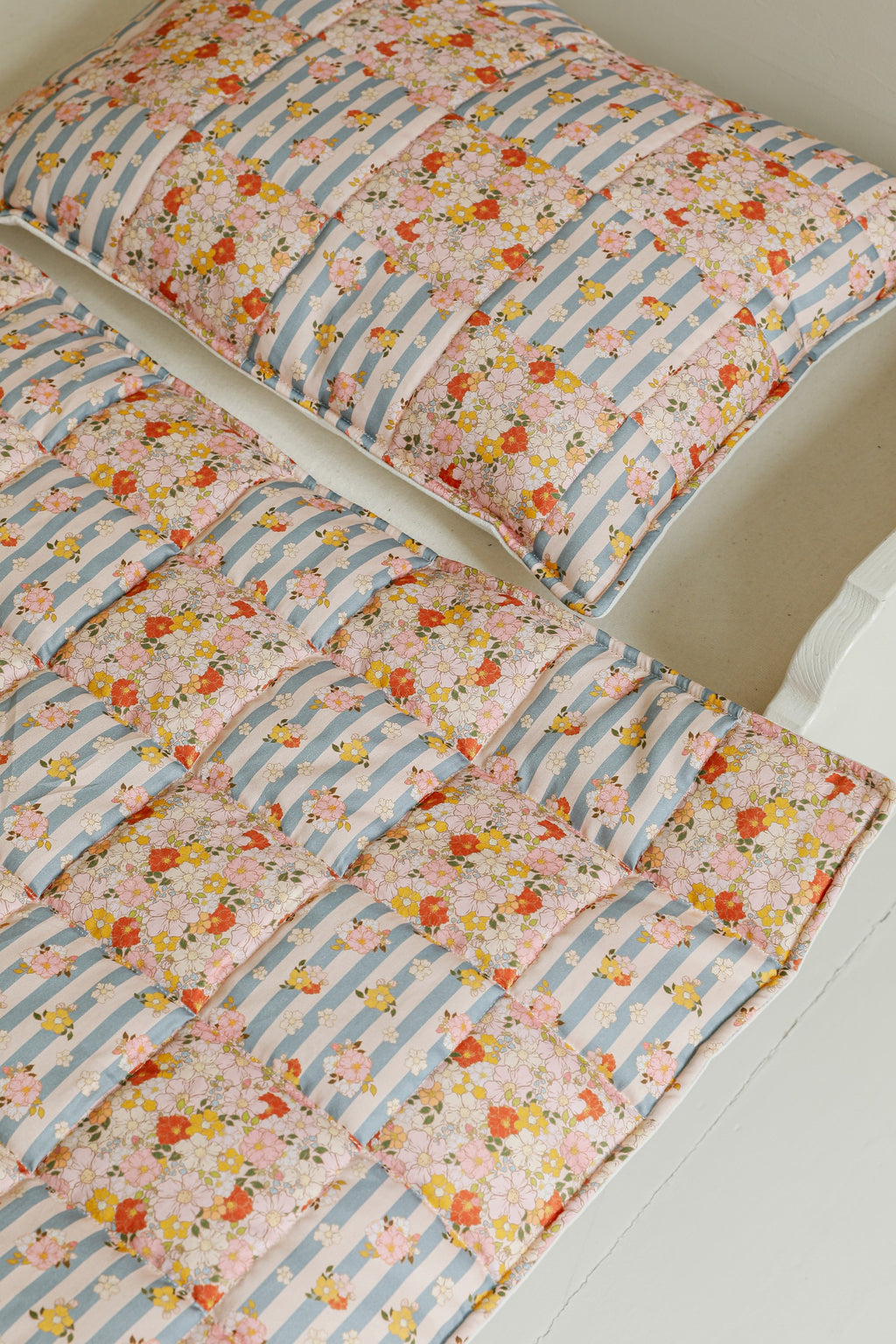 cotton quilted patchwork blanket and pillow set laid flat on a wooden floor, showcasing summer garden patterns