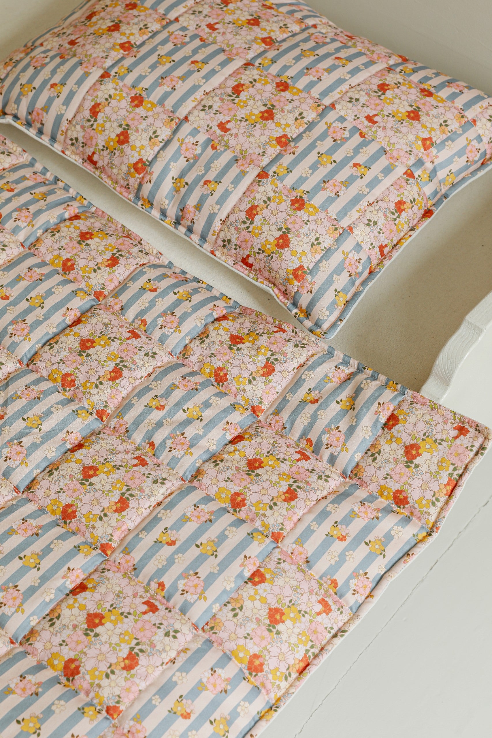 cotton quilted patchwork blanket and pillow set laid flat on a wooden floor, showcasing summer garden patterns
