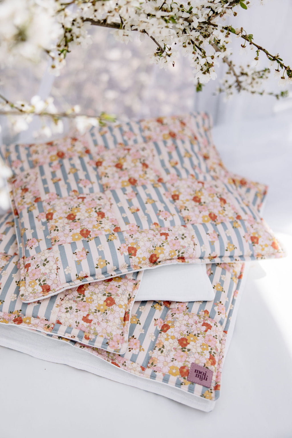 soft cotton quilted patchwork blanket and pillow set in summer garden print, laid out on a wooden floor with natural sunlight