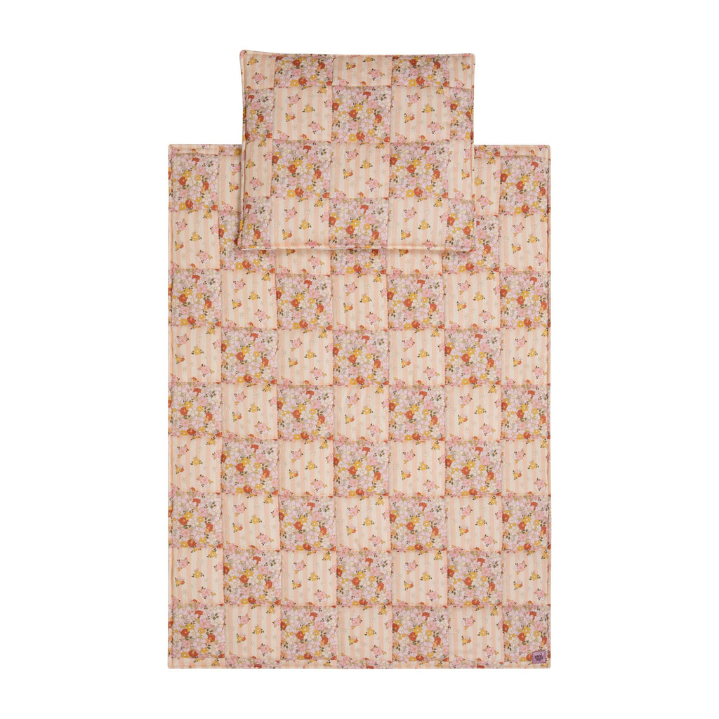 playful spring garden cotton quilted blanket and pillow set laid on grass, bright patchwork patterns under sunlight