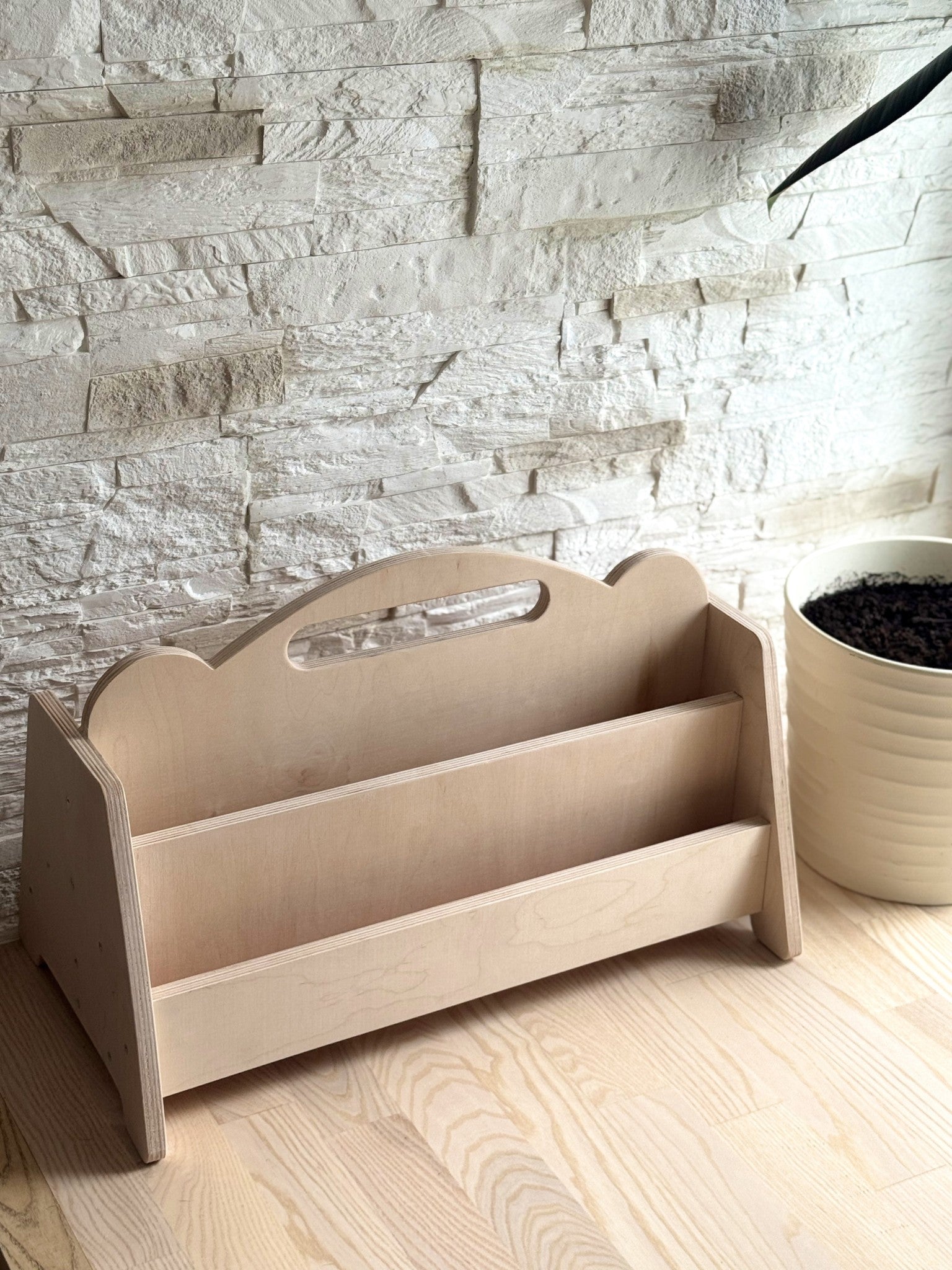 a close-up view of the birch plywood bookshelf in a bright room, showing the practical side grips and accessible shelf height for a child