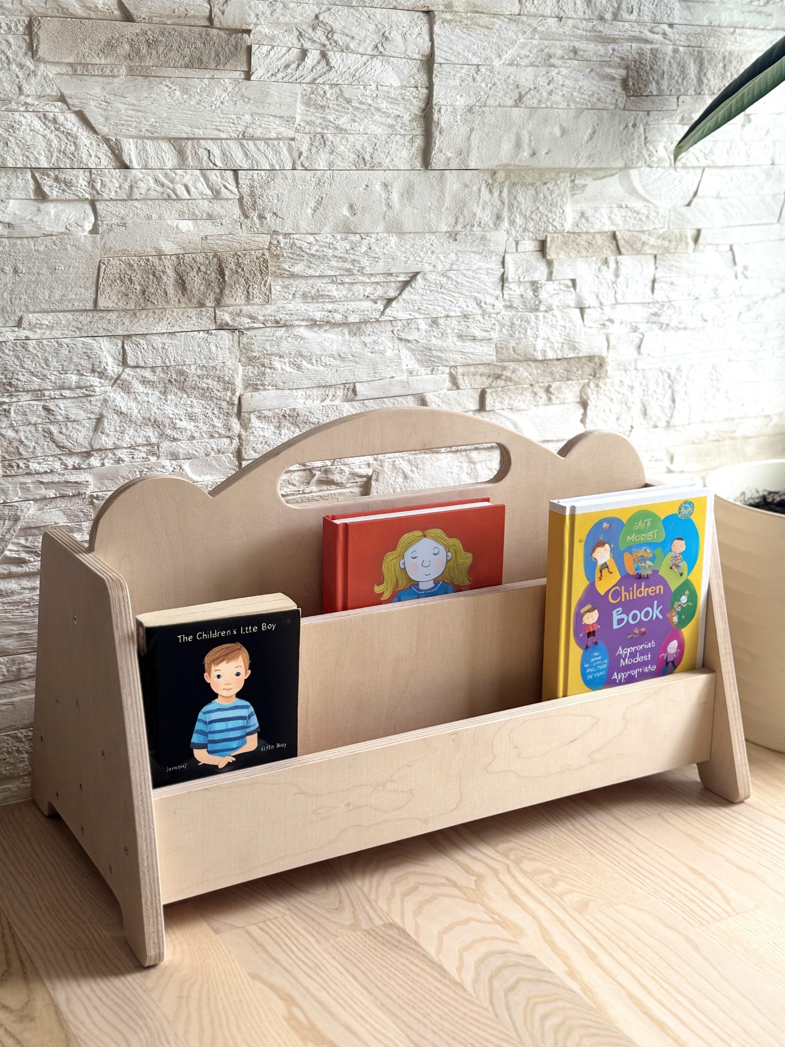 a low-angle view of the birch bookshelf in a sunlit nursery corner, showcasing its accessible height for toddlers