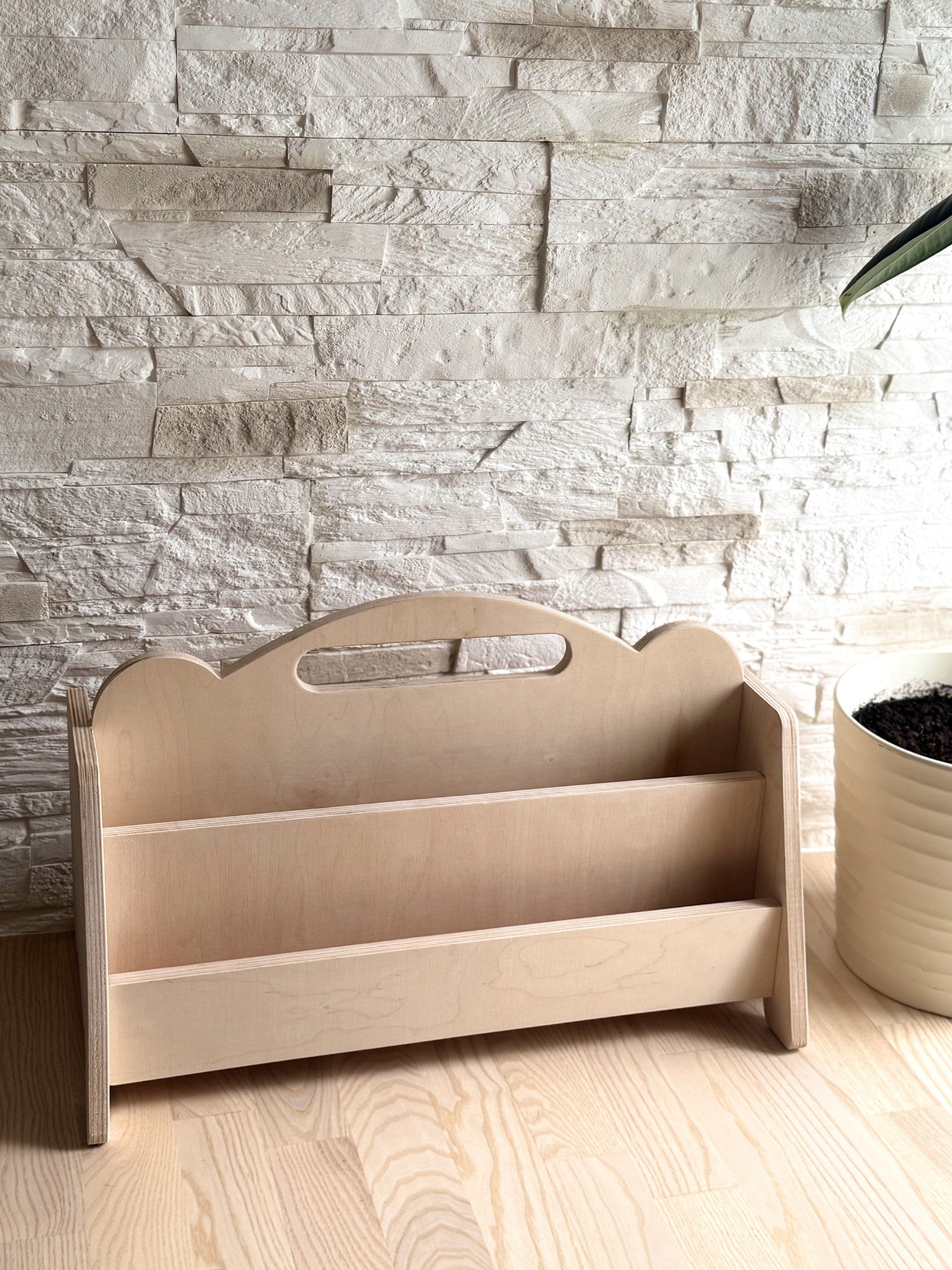 a child's hand selecting a book from the low birch plywood shelf in a sunlit nursery