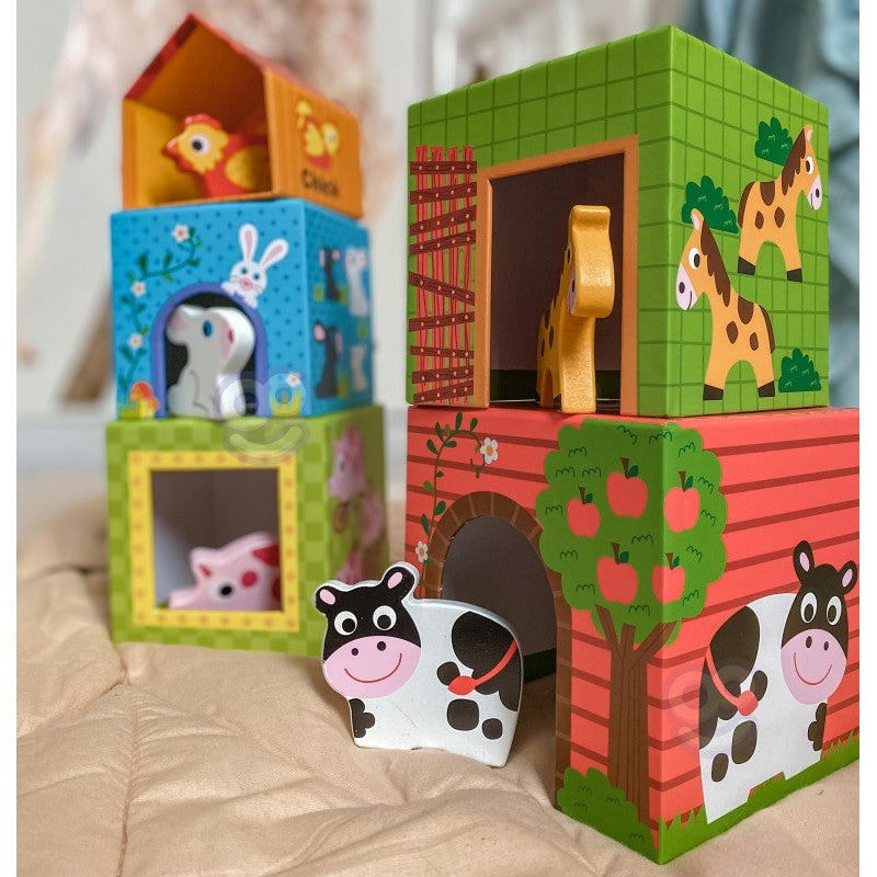 a child's hand stacking a green farm cube puzzle with a wooden cow peeking out