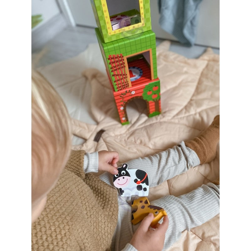a child's hand stacking a green cube with a cow illustration in a sunlit playroom