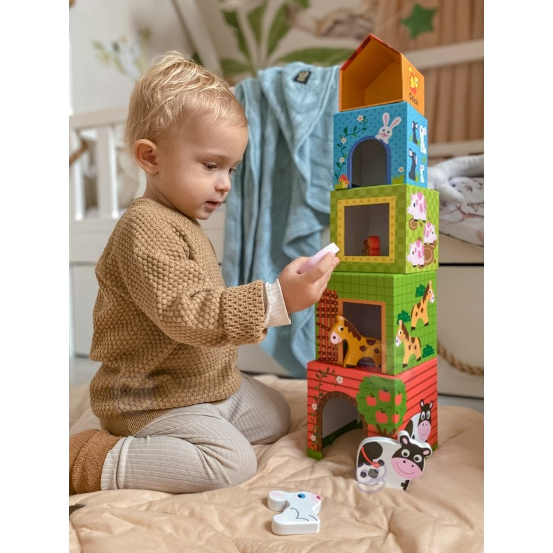 a child's hand stacking the largest farm cube with a happy pig figurine on top