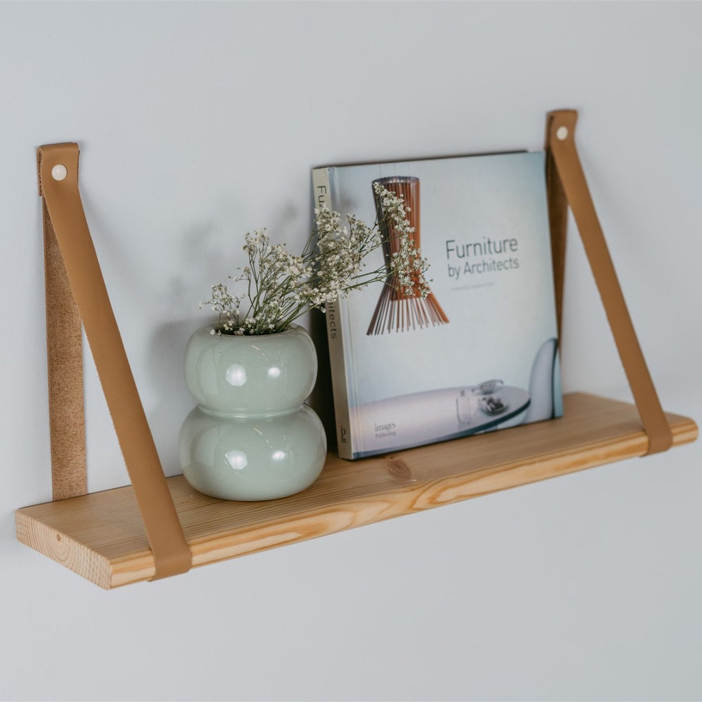 a soft-lit floating shelf with camel leather straps in a cozy reading nook