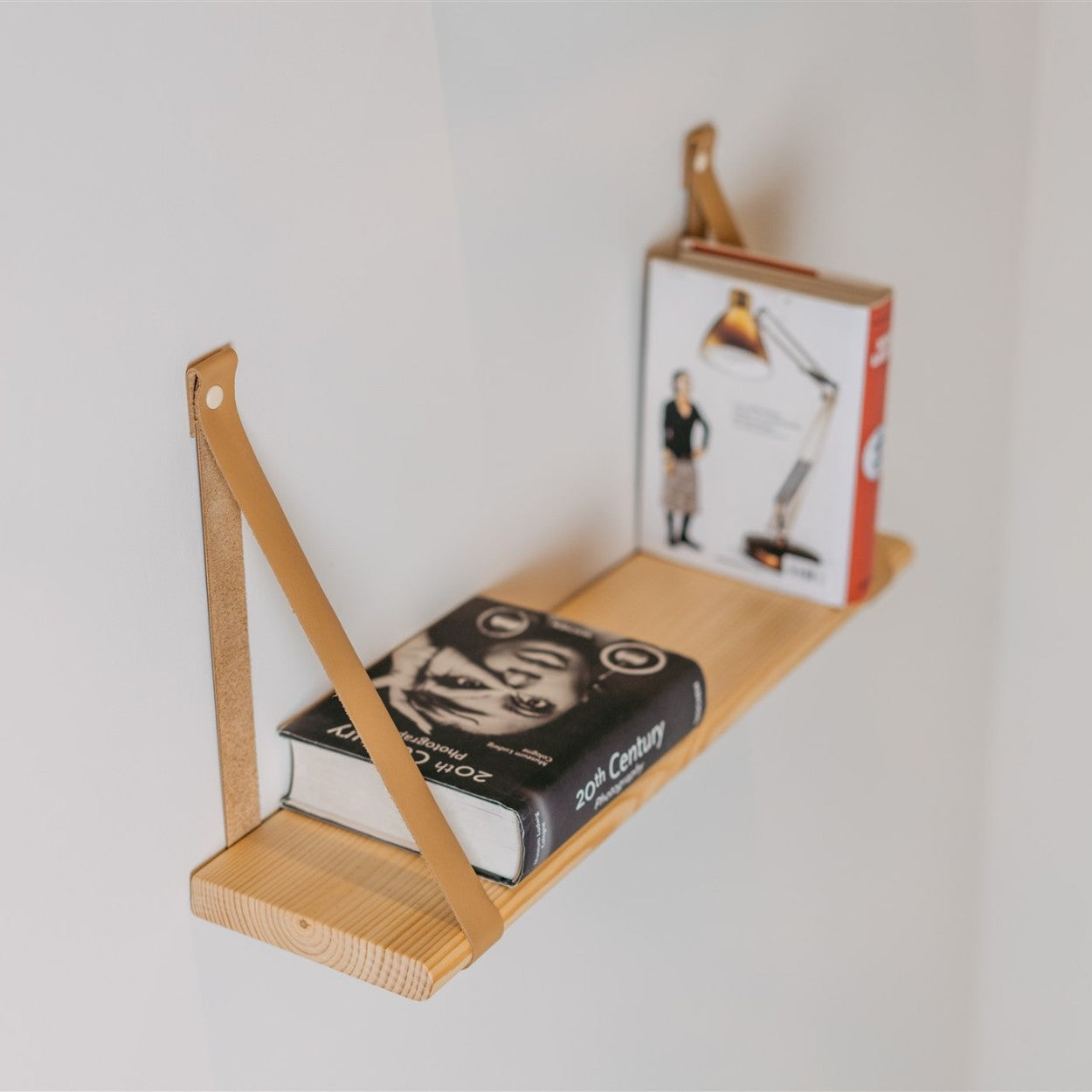 bold 60 cm solid pine floating shelf with light camel leather straps in dramatic low-light setting