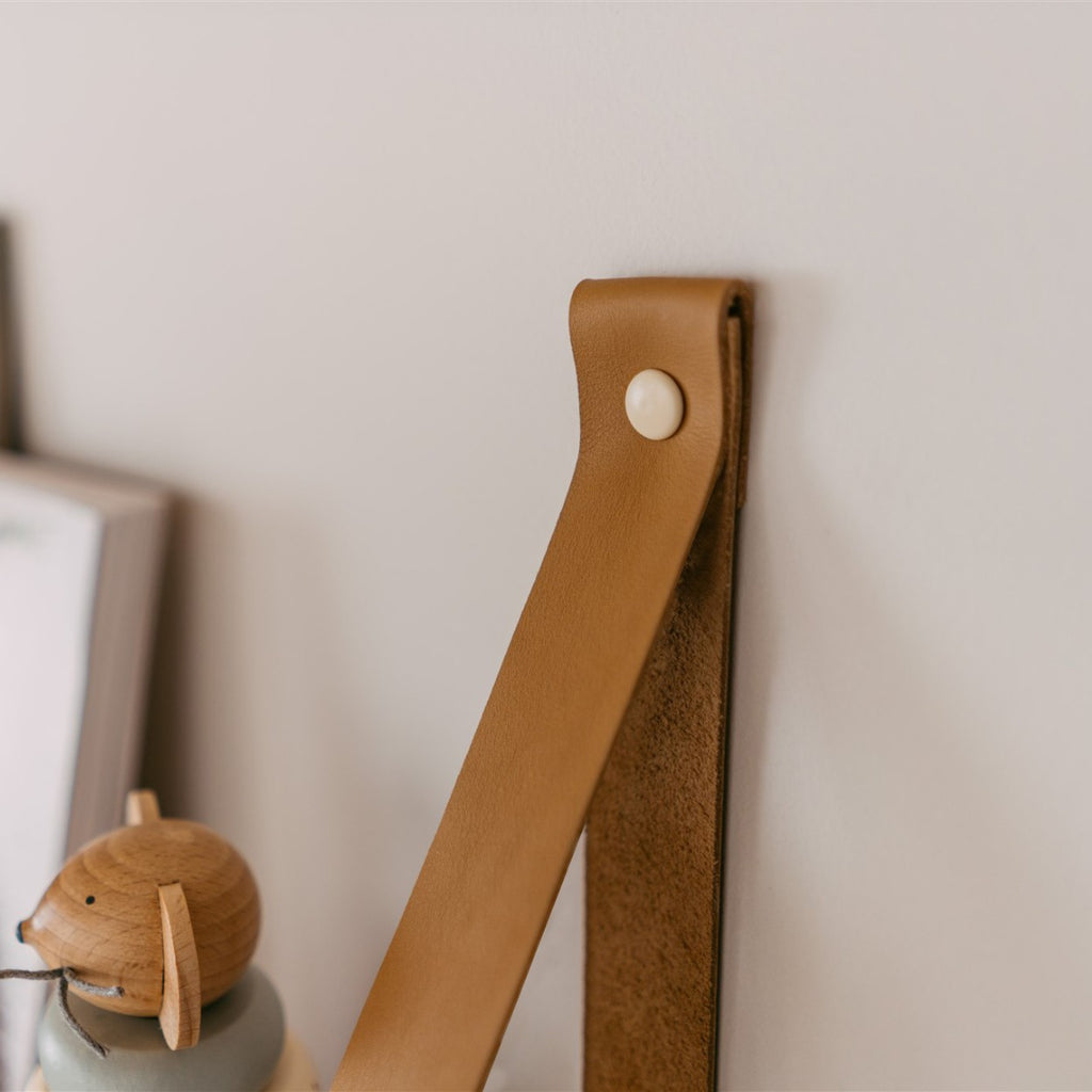 a functional 70 cm pine shelf with leather straps holding a stack of soft cotton baby clothes
