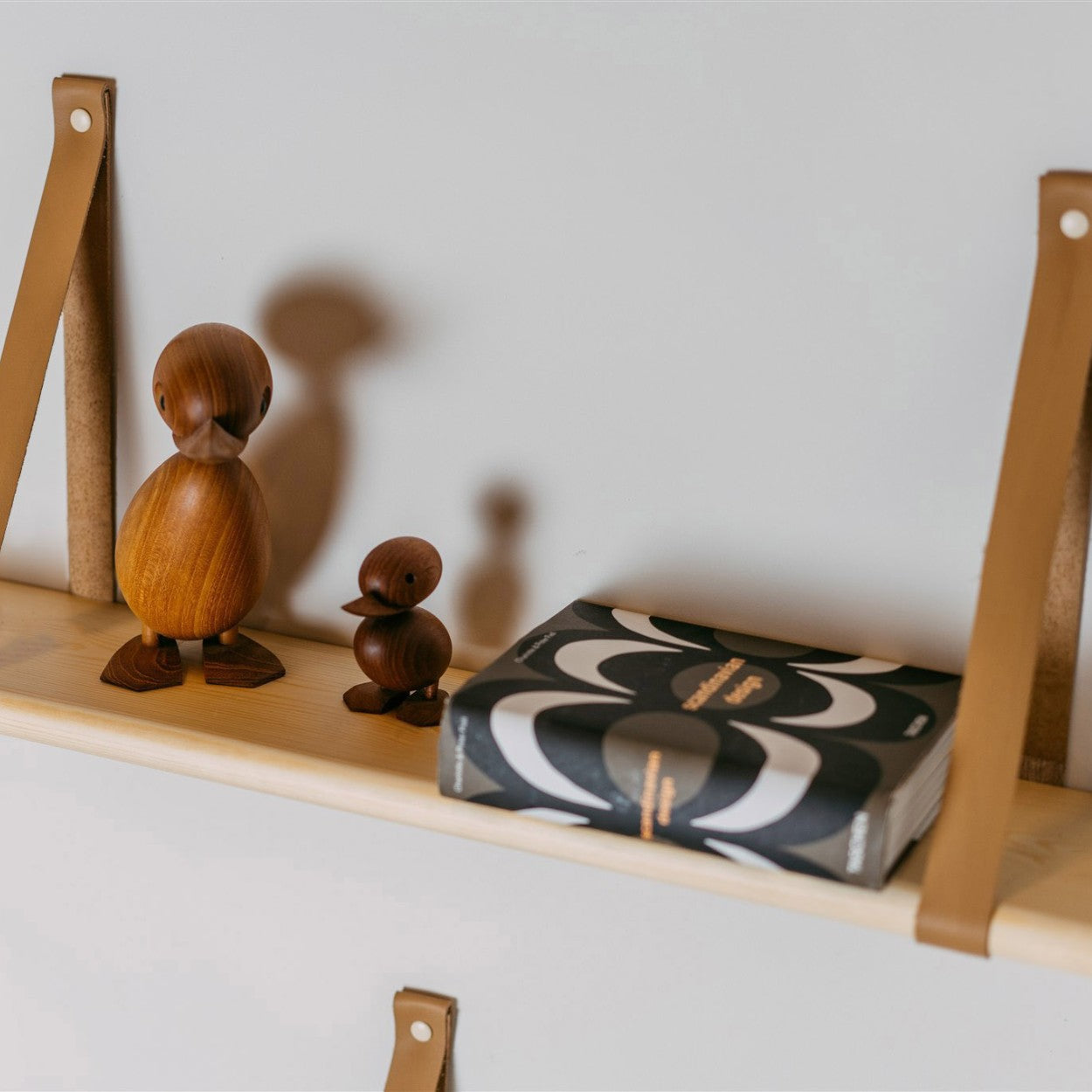 a practical 70 cm floating pine shelf with leather straps holding a stack of baby clothing