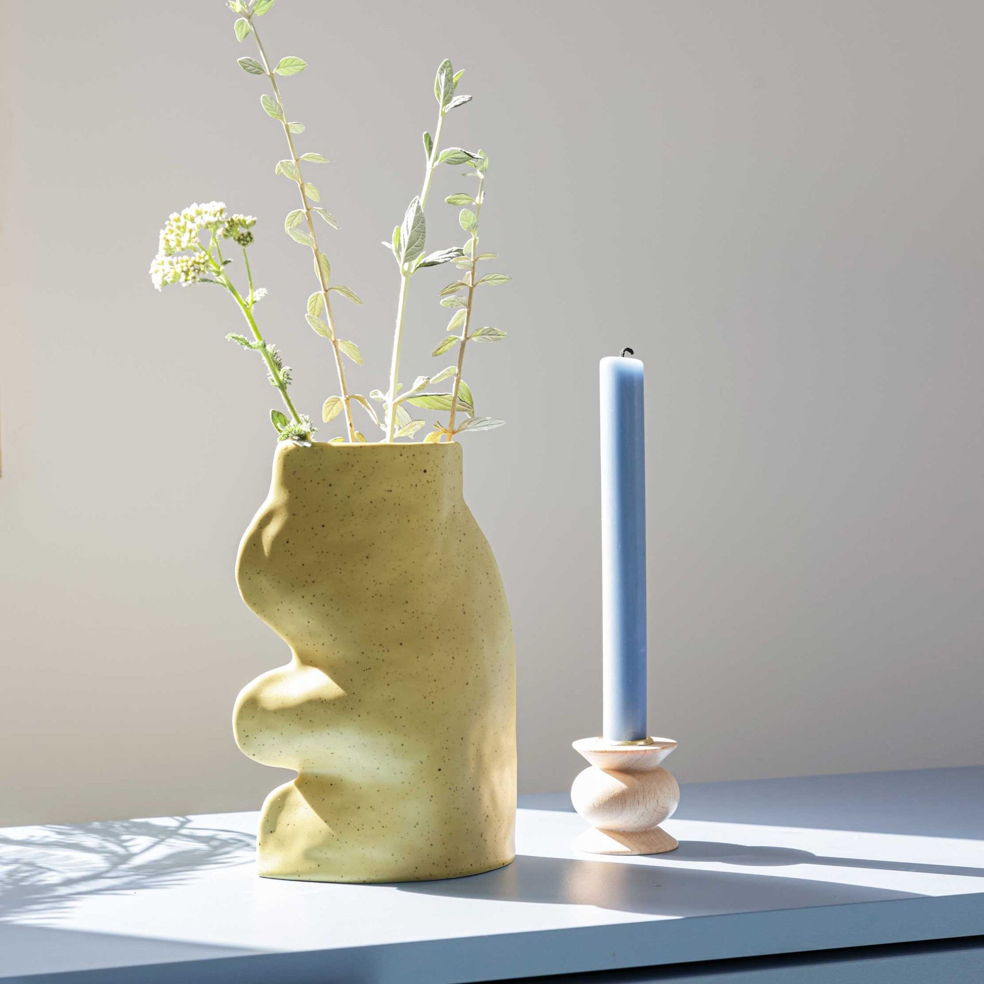 playful pistachio ceramic vase on a sunlit windowsill with a single wildflower